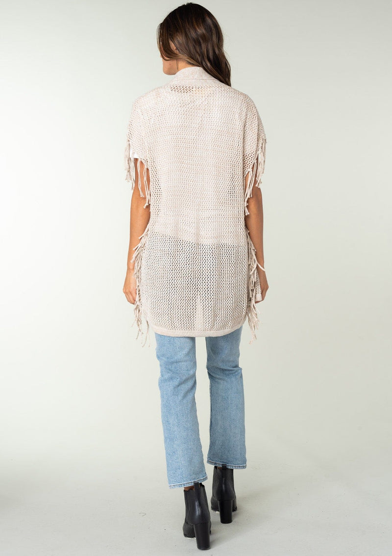 [Color: Bone] A back facing image of a brunette model wearing a open knit lightweight cardigan with fringe accents. An easy throw on for casual outings. 