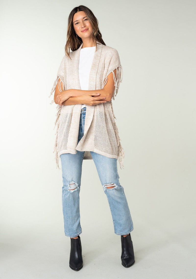 [Color: Bone] A front facing image of a brunette model wearing a open knit lightweight cardigan with fringe accents. An easy throw on for casual outings. 