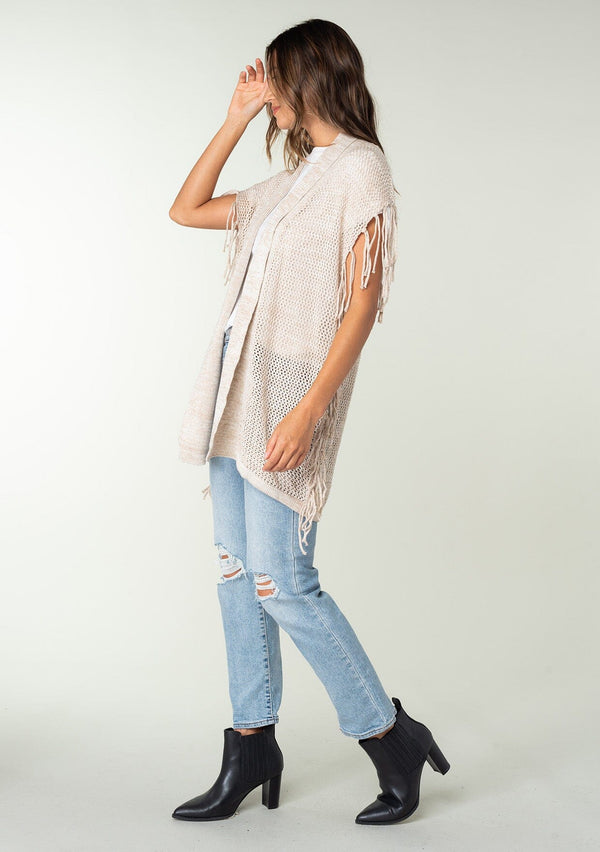 [Color: Bone] A side facing image of a brunette model wearing a open knit lightweight cardigan with fringe accents. An easy throw on for casual outings. 