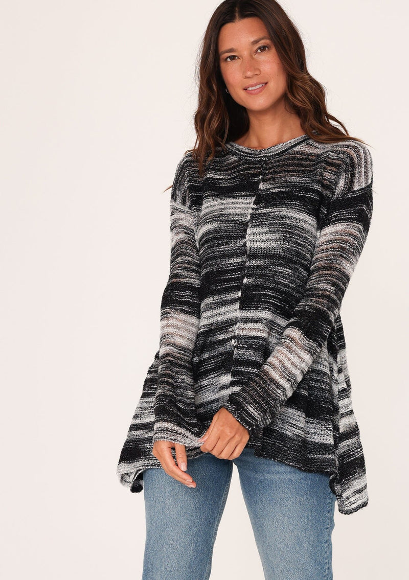 [Color: Black/Grey] A front facing image of a brunette model wearing a relaxed melange knit sweater. This lightweight sweater features a round neckline, a swing hem, and comfortable long sleeves with dropped shoulders. 