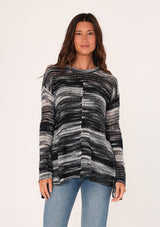 [Color: Black/Grey] A front facing image of a brunette model wearing a relaxed melange knit sweater. This lightweight sweater features a round neckline, a swing hem, and comfortable long sleeves with dropped shoulders. 