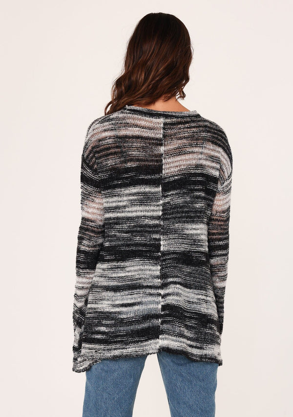 [Color: Black/Grey] A back facing image of a brunette model wearing a relaxed melange knit sweater. This lightweight sweater features a round neckline, a swing hem, and comfortable long sleeves with dropped shoulders. 