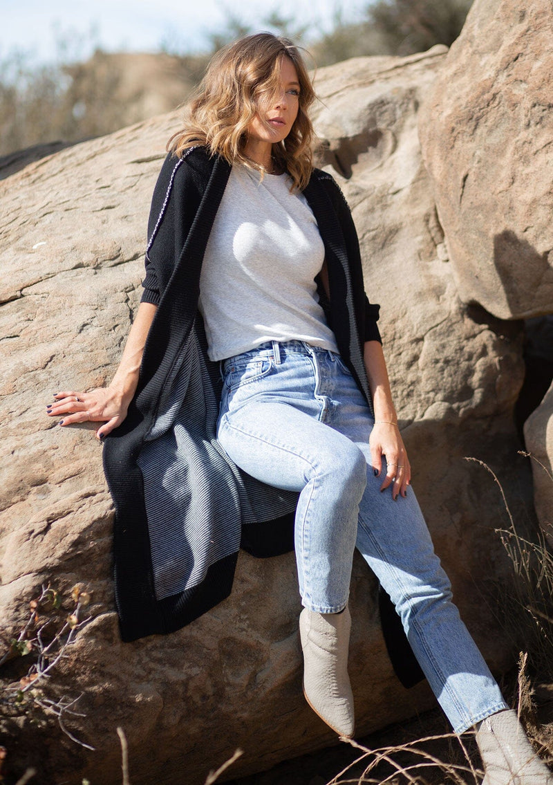 [Color: Black] A blonde model wearing a fall black cardigan with a contrast interior, exposed seam details, and a tapered sleeve at the elbow. 