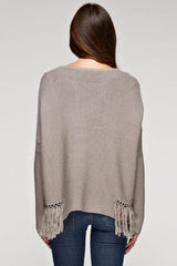 [Color: Mushroom] A back facing image of a brunette model wearing a grey knit pullover with side fringe details, long sleeves with dropped shoulders, and a round neckline. 