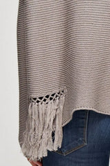 [Color: Mushroom] A detail image of a brunette model wearing a grey knit pullover with side fringe details, long sleeves with dropped shoulders, and a round neckline. 
