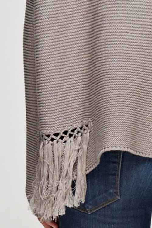 [Color: Mushroom] A detail image of a brunette model wearing a grey knit pullover with side fringe details, long sleeves with dropped shoulders, and a round neckline. 