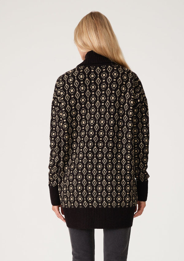 [Color: Black/Taupe] A back facing image of a blonde model wearing a cozy bohemian cardigan in a black and taupe geo jacquard design. With contrast ribbed trim, side pockets, a shawl collar, and a toggle button closure. 