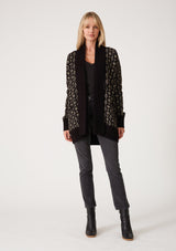 [Color: Black/Taupe] A full body front facing image of a blonde model wearing a cozy bohemian cardigan in a black and taupe geo jacquard design. With contrast ribbed trim, side pockets, a shawl collar, and a toggle button closure. 