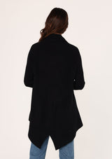 [Color: Black] A back facing image of a brunette model wearing a black shawl cardigan with a ribbed texture, open front, and a back vent detail. Cozy and relaxed for the fall season. 