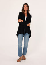 [Color: Black] A front facing image of a brunette model wearing a black shawl cardigan with a ribbed texture, open front, and a back vent detail. Cozy and relaxed for the fall season. 