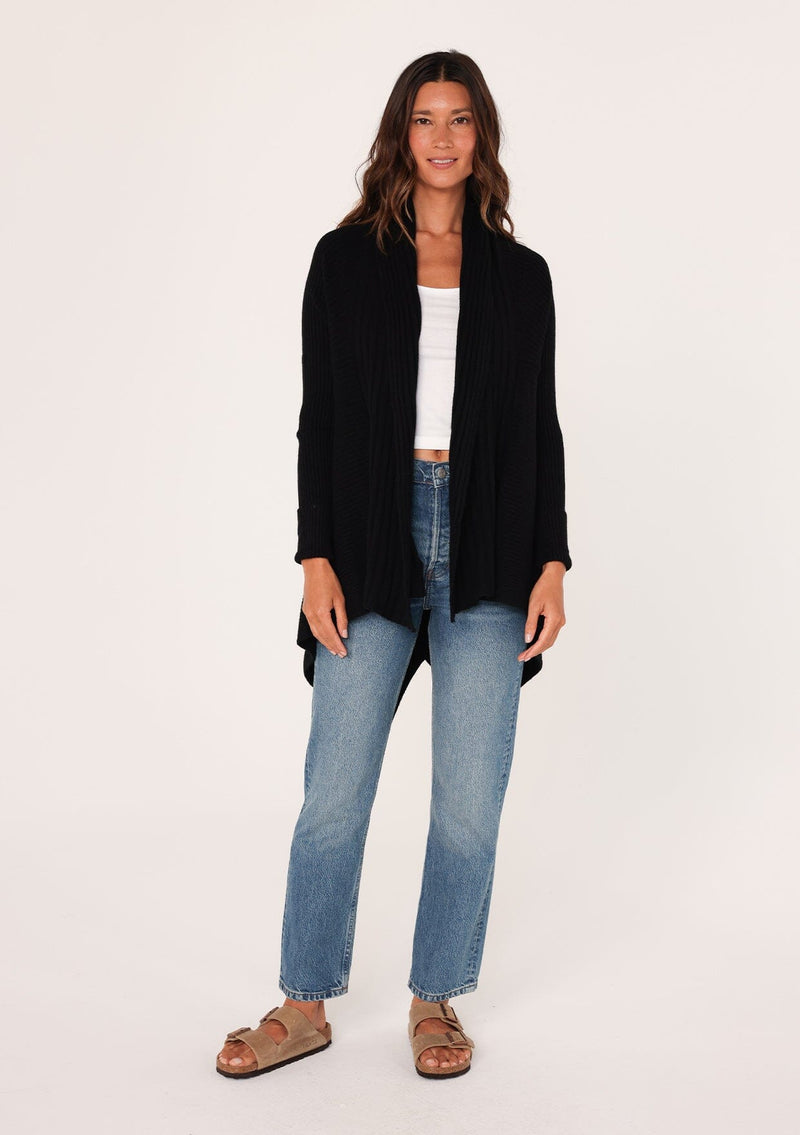 [Color: Black] A front facing image of a brunette model wearing a black shawl cardigan with a ribbed texture, open front, and a back vent detail. Cozy and relaxed for the fall season. 