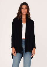[Color: Black] A front facing image of a brunette model wearing a black shawl cardigan with a ribbed texture, open front, and a back vent detail. Cozy and relaxed for the fall season. 
