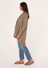 [Color: Mushroom] A side facing image of a brunette model wearing a brown shawl cardigan with a ribbed texture, open front, and a back vent detail. Cozy and relaxed for the fall season. 