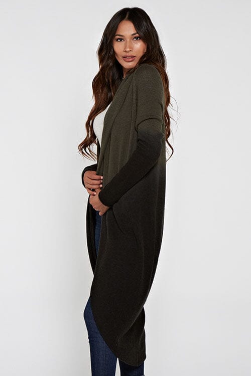 [Color: Olive/Black] A side facing image of a blonde model wearing a dip dyed cocoon cardigan with a shawl collar and long sleeves. A versatile cardigan that can transition from a duster to a mid-length cardigan. 