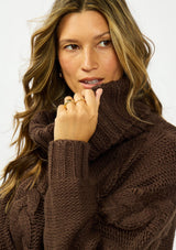 [Color: Chocolate] A detail image of a brunette model wearing a dark brown cable knit sweater with a turtleneck. 