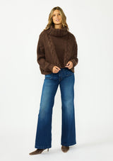 [Color: Chocolate] A front facing image of a brunette model wearing a dark brown cable knit sweater with a turtleneck. Styled with dark wash denim and brown boots. 