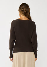 [Color: Dark Brown] A back facing image of a blonde model wearing a brown waffle knit pullover sweater. With long sleeves, a relaxed fit, and a wide neckline that can be worn off the shoulder.