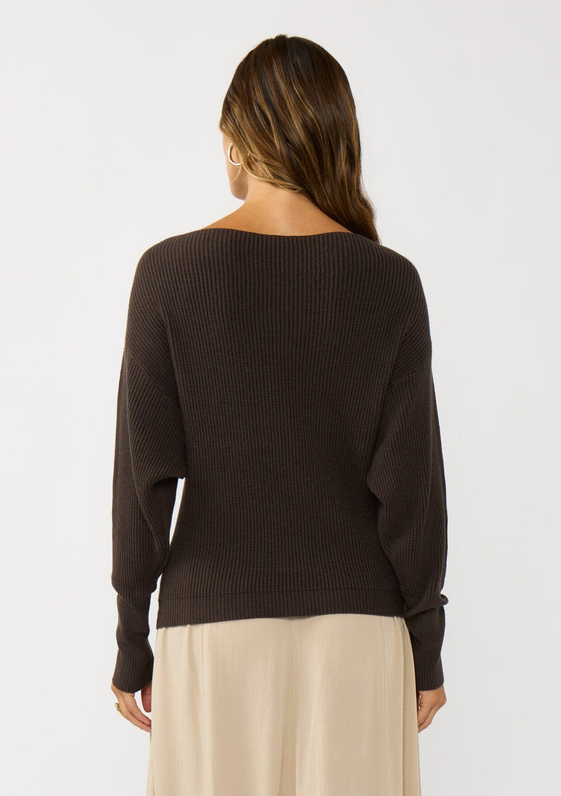 [Color: Dark Brown] A back facing image of a blonde model wearing a brown waffle knit pullover sweater. With long sleeves, a relaxed fit, and a wide neckline that can be worn off the shoulder.