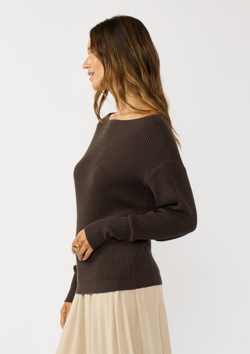 [Color: Dark Brown] A side facing image of a blonde model wearing a brown waffle knit pullover sweater. With long sleeves, a relaxed fit, and a wide neckline that can be worn off the shoulder.