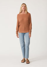 [Color: Clay] A full body front facing image of a blonde model wearing a clay brown waffle knit pullover sweater. With long sleeves, a relaxed fit, and a wide neckline that can be worn off the shoulder.