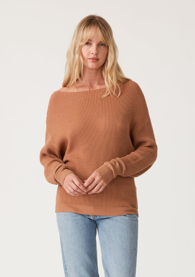[Color: Clay] A front facing image of a blonde model wearing a clay brown waffle knit pullover sweater. With long sleeves, a relaxed fit, and a wide neckline that can be worn off the shoulder.
