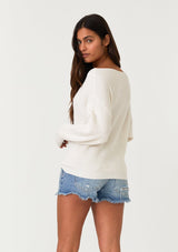 [Color: Natural] A back facing image of a brunette model wearing an off white waffle knit pullover sweater. With long sleeves, a relaxed fit, and a wide neckline that can be worn off the shoulder.