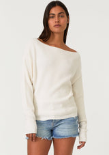 [Color: Natural] A front facing image of a brunette model wearing an off white waffle knit pullover sweater. With long sleeves, a relaxed fit, and a wide neckline that can be worn off the shoulder.