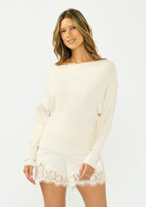 [Color: Natural] A front facing image of a brunette model wearing an off white pullover sweater with a boat neckline and long sleeves that taper at the cuffs. Styled with off white satin lace shorts. 
