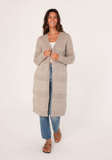 [Color: Oatmeal] A front view of a brunette woman modeling a long, open-front beige mélange knit cardigan over a white top and blue jeans.