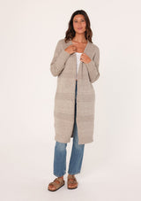 [Color: Oatmeal] A front view of a brunette woman modeling a long, open-front beige mélange knit cardigan over a white top and blue jeans.