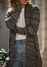 [Color: Heather Charcoal/Brown] A blonde model wearing a grey and brown melange stripe cardigan. Featuring a cozy shawl collar and front patch pockets. Perfect for casual fall outings. 