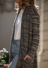 [Color: Heather Charcoal/Brown] A blonde model wearing a grey and brown melange stripe cardigan. Featuring a cozy shawl collar and front patch pockets. Perfect for casual fall outings. 