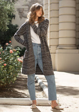 [Color: Heather Charcoal/Brown] A blonde model wearing a grey and brown melange stripe cardigan. Featuring a cozy shawl collar and front patch pockets. Perfect for casual fall outings. 