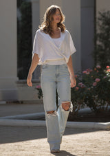 [Color: Heather Off White] A front facing image of a blonde model wearing a pointelle knit sweater top with a surplice v-neckline, short dolman sleeves,  wide sleeve openings, and fitted ribbed hem. 