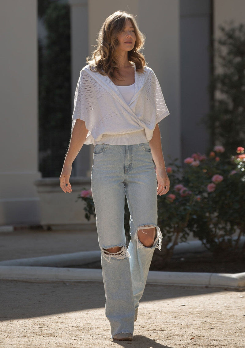 [Color: Heather Off White] A front facing image of a blonde model wearing a pointelle knit sweater top with a surplice v-neckline, short dolman sleeves,  wide sleeve openings, and fitted ribbed hem. 