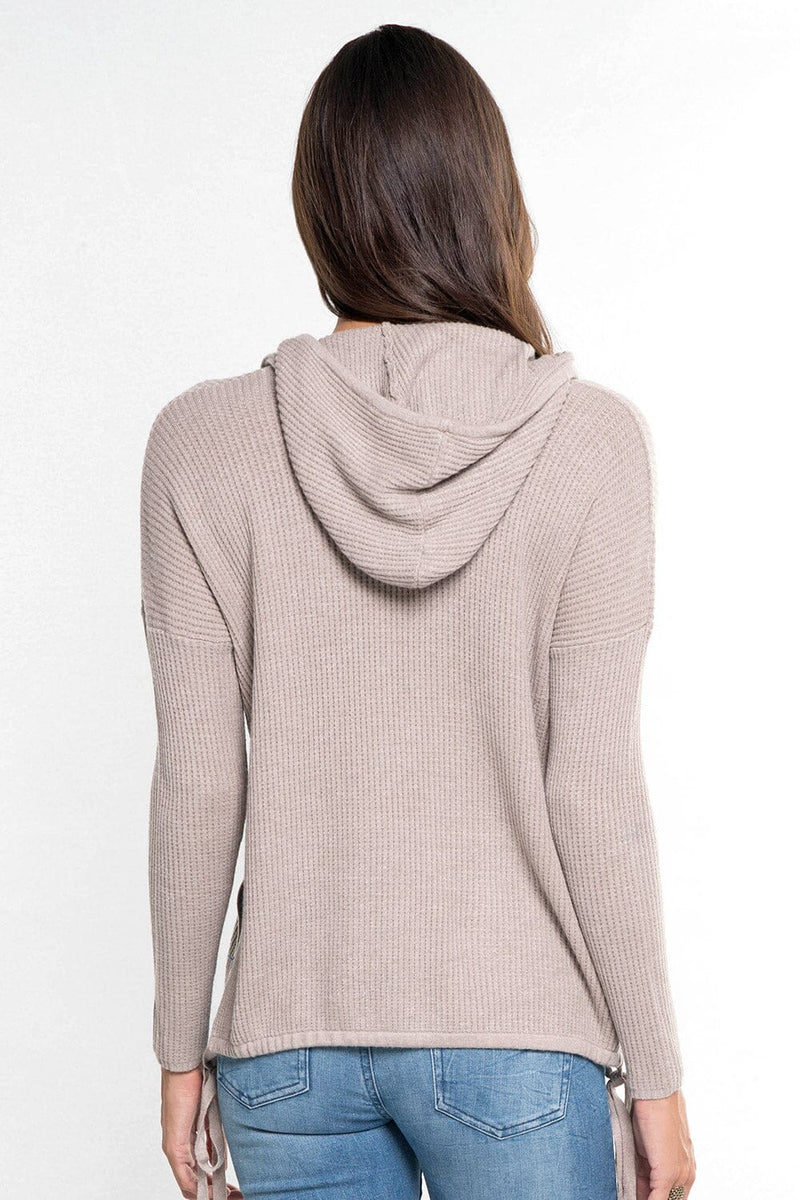 [Color: Heather Cement] A back facing image of a brunette model wearing a taupe waffle knit pullover with a drawstring hoodie, kangaroo pockets, and side slits with tie detail. 