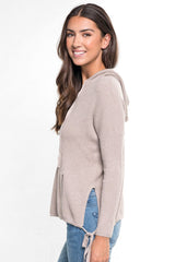 [Color: Heather Cement] A side facing image of a brunette model wearing a taupe waffle knit pullover with a drawstring hoodie, kangaroo pockets, and side slits with tie detail. 