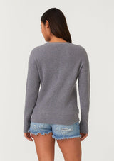 [Color: Heather Charcoal] A back facing image of a brunette model wearing a heather grey waffle knit pullover sweater. With long sleeves, a wide crew neckline, and a twist front detail at the waist.