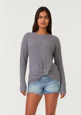 [Color: Heather Charcoal] A half body front facing image of a brunette model wearing a heather grey waffle knit pullover sweater. With long sleeves, a wide crew neckline, and a twist front detail at the waist.