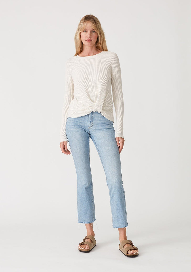 [Color: Natural] A full body front facing image of a blonde model wearing an ivory waffle knit pullover sweater. With long sleeves, a wide crew neckline, and a twist front detail at the waist. 