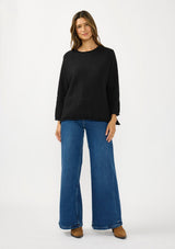 [Color: Black] Afront facing image of a brunette model wearing a relaxed black honeycomb knit sweater with a round neckline, side vents and rolled edges.