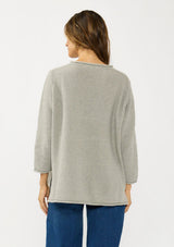 [Color: Cement] A back facing image of a brunette model wearing a relaxed grey honeycomb knit sweater with a round neckline, side vents and rolled edges.