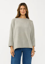 [Color: Cement] A front facing image of a brunette model wearing a relaxed grey honeycomb knit sweater with a round neckline, side vents and rolled edges.