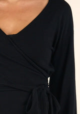 [Color: Black] A detail image of a brunette model wearing a casual black wrap front top with long flowy sleeves, a v neckline, and an adjustable waist tie. 