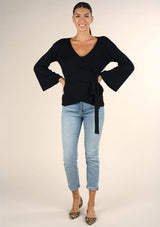 [Color: Black] A brunette model wearing a casual black wrap front top with long flowy sleeves, a v neckline, and an adjustable waist tie. 