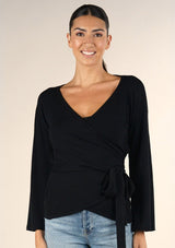 [Color: Black] A brunette model wearing a casual black wrap front top with long flowy sleeves, a v neckline, and an adjustable waist tie. 