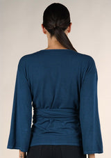 [Color: Dark Sapphire] A brunette model wearing a casual blue wrap front top with long flowy sleeves, a v neckline, and an adjustable waist tie. 