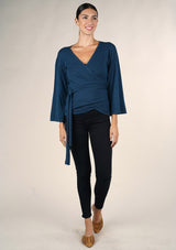 [Color: Dark Sapphire] A front facing image o of a brunette model wearing a casual blue wrap front top with long flowy sleeves, a v neckline, and an adjustable waist tie. 