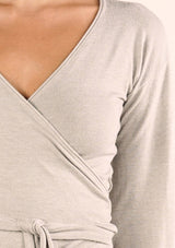 [Color: Heather Stone] A detail image of a brunette model wearing a casual wrap front top with long flowy sleeves, a v neckline, and an adjustable waist tie. 