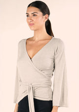 [Color: Heather Stone] A side facing image of a brunette model wearing a casual wrap front top with long flowy sleeves, a v neckline, and an adjustable waist tie. 